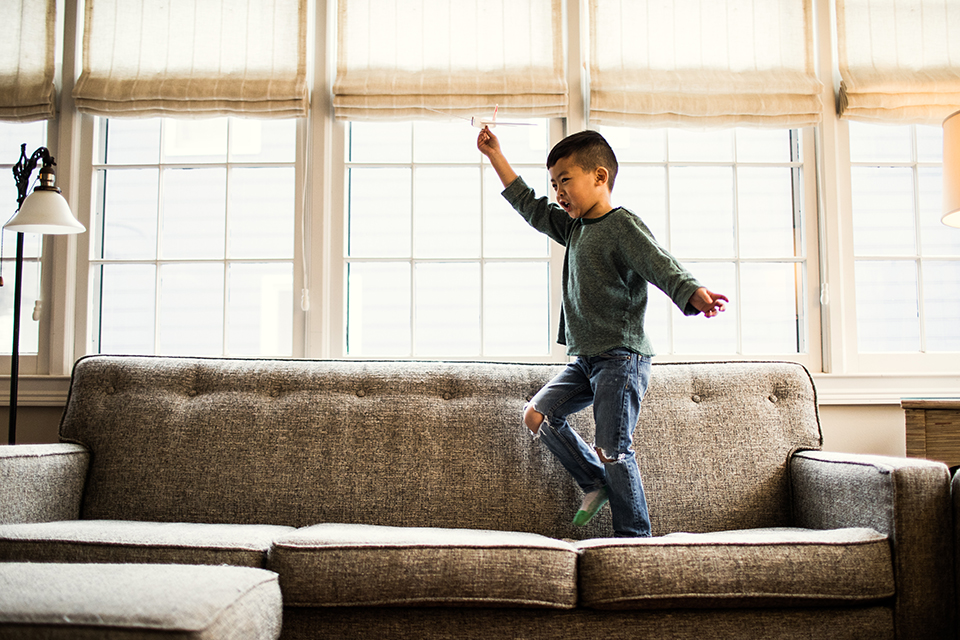 Boy jumping on sofa in front of living room windows