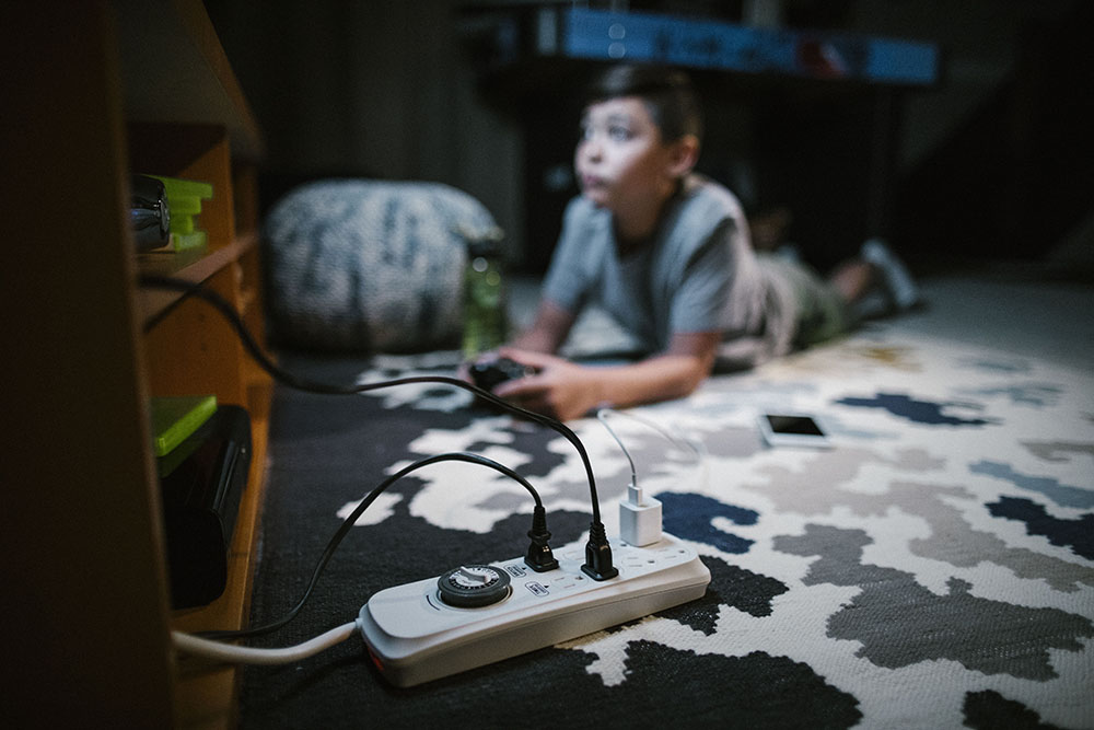 Young boy playing video games with console plugged into a loaded power bar