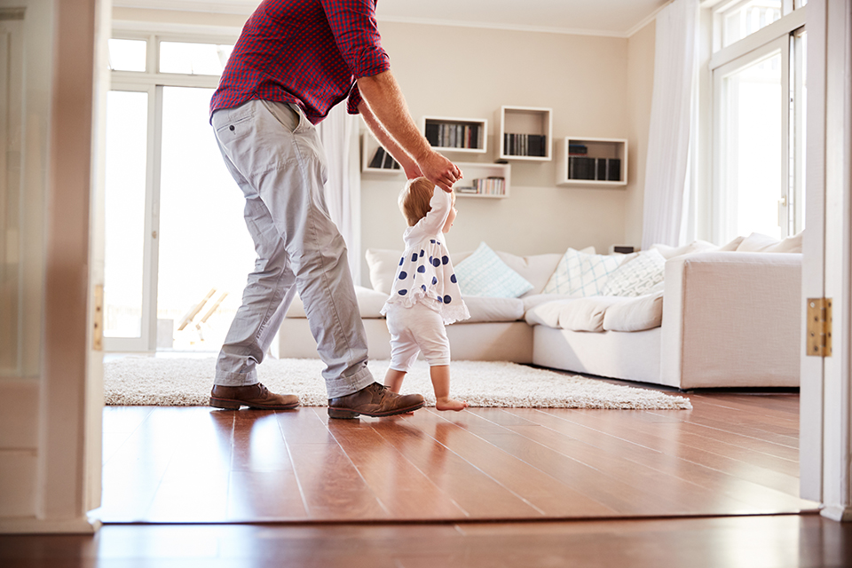father helping child walking across living room